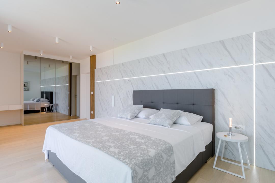 A big bedroom with a mirror-closet, a king-sized bed and a wall that is backlit with LED's